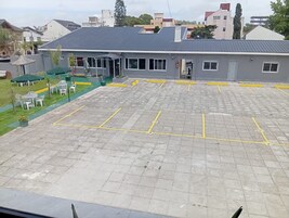 Un estacionamiento con espacios delimitados, un edificio de techo plano y una zona verde con mobiliario exterior.