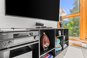 A home theater system with a flat-screen TV, audio components, and a bookshelf with children's toys and decorative items. - Skiers' Paradise in Keystone | 4BR Luxury Retreat | Shuttle Steps Away (Keystone)