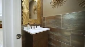 A bathroom with a white sink, dark wooden cabinet, and a decorative mirror with a sunburst pattern. - The Grand Estate (Elkins Park)