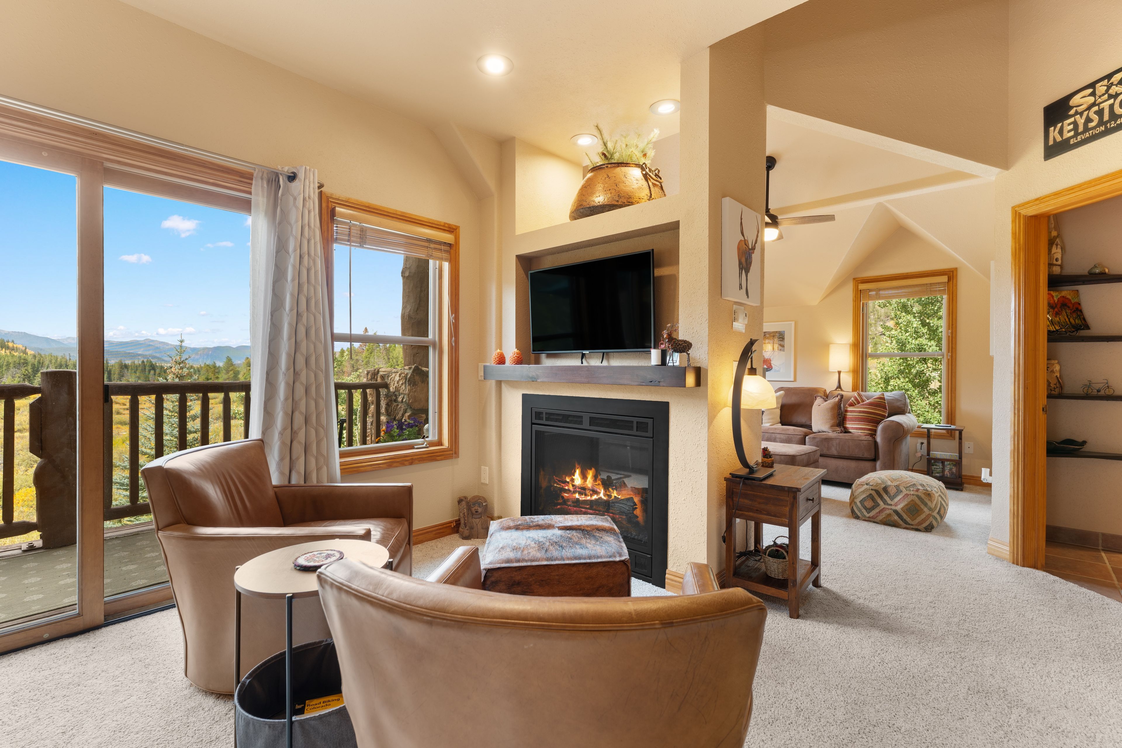 A spacious living room with a fireplace, a television, and a balcony with a scenic view.