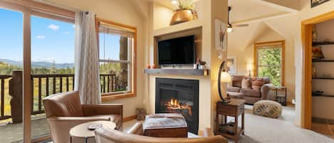 A spacious living room with a fireplace, a television, and a balcony with a scenic view.