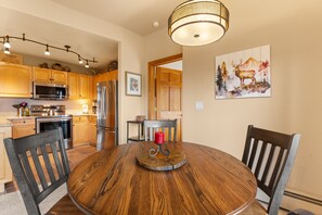 A kitchen with wooden cabinets, stainless steel appliances, and a dining area with a round wooden table and chairs. - Keystone Getaway at Hidden River Lodge – Balcony Views & Shared Hot Tub (Keystone)