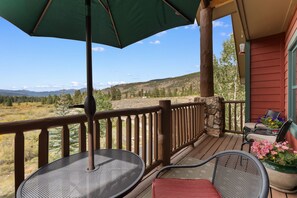 A wooden deck with a table and chairs, an umbrella, and a view of a mountainous landscape. - Keystone Getaway at Hidden River Lodge – Balcony Views & Shared Hot Tub (Keystone)