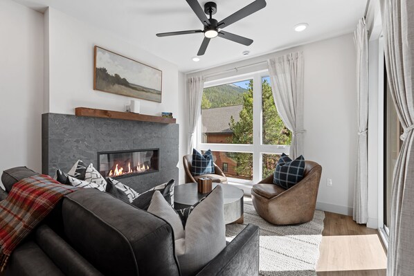 Ein modernes Wohnzimmer mit Kamin, Ledersofas und einem großen Fenster mit Bergblick.