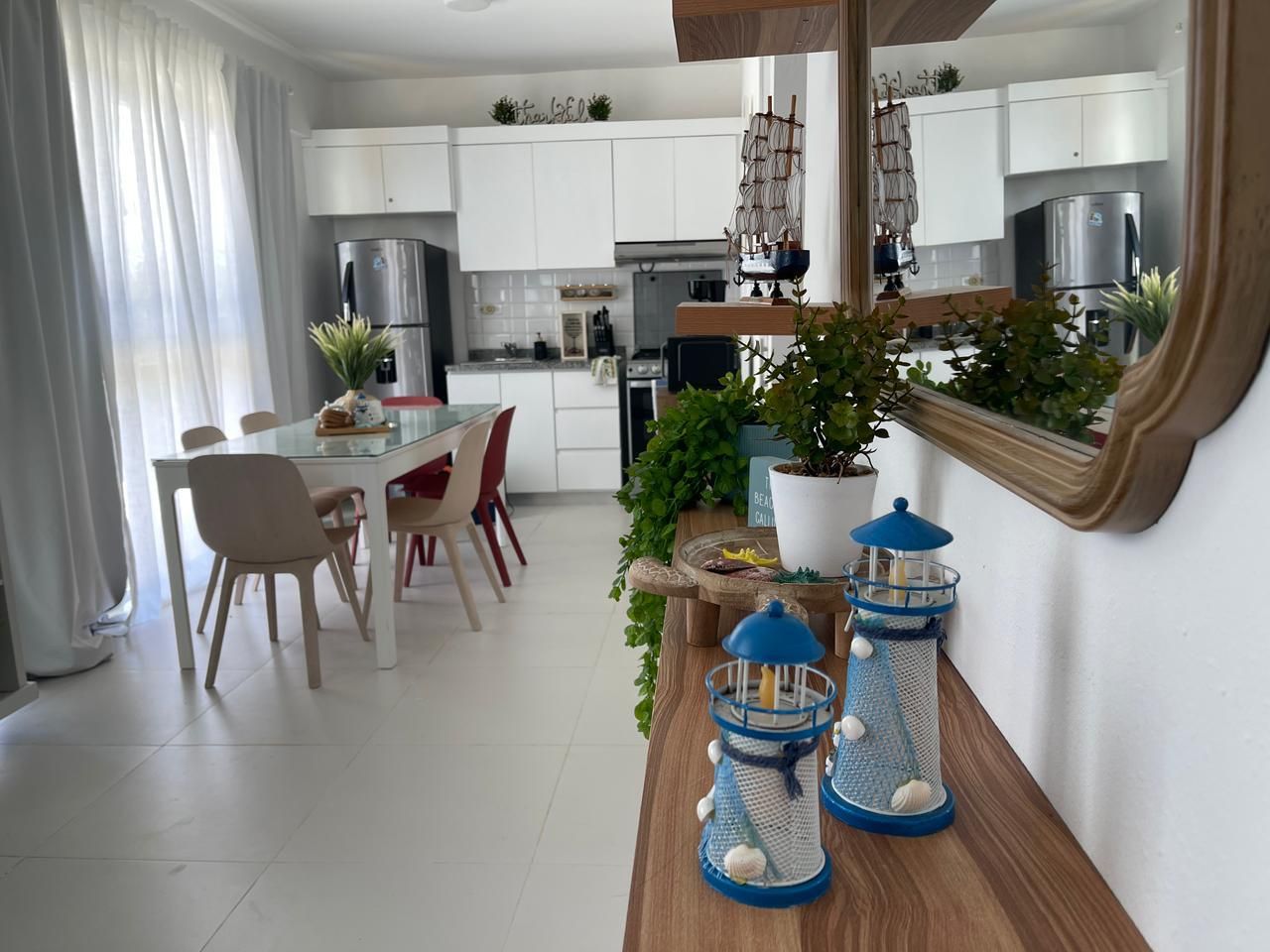 Una cocina moderna con armarios blancos, electrodomésticos de acero inoxidable y un comedor con mesa y sillas de vidrio.