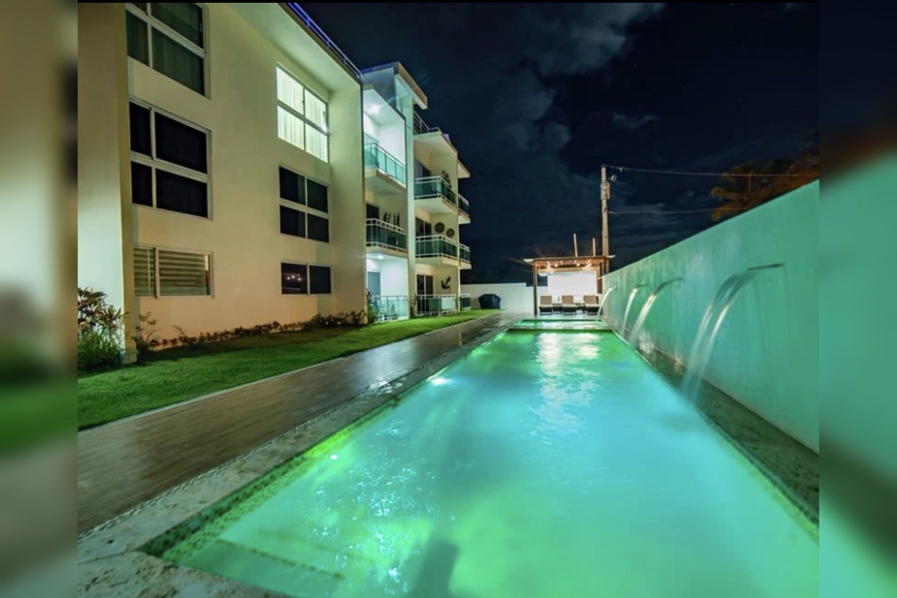 Ein Pool mit einem modernen Gebäude an einer Seite und einem überdachten Bereich auf der anderen Seite.