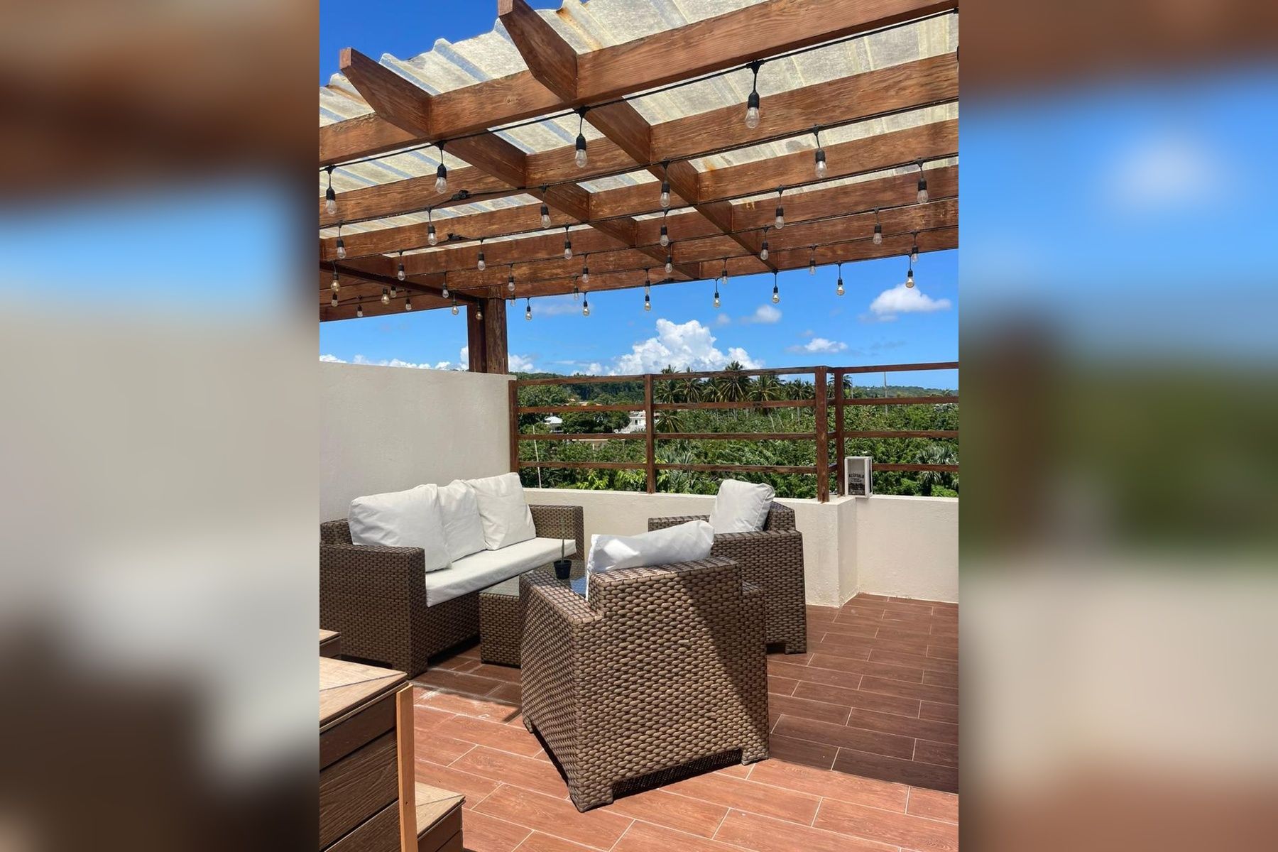 Eine Terrasse im Freien mit Korbmöbeln und einer darüberliegenden Pergola.