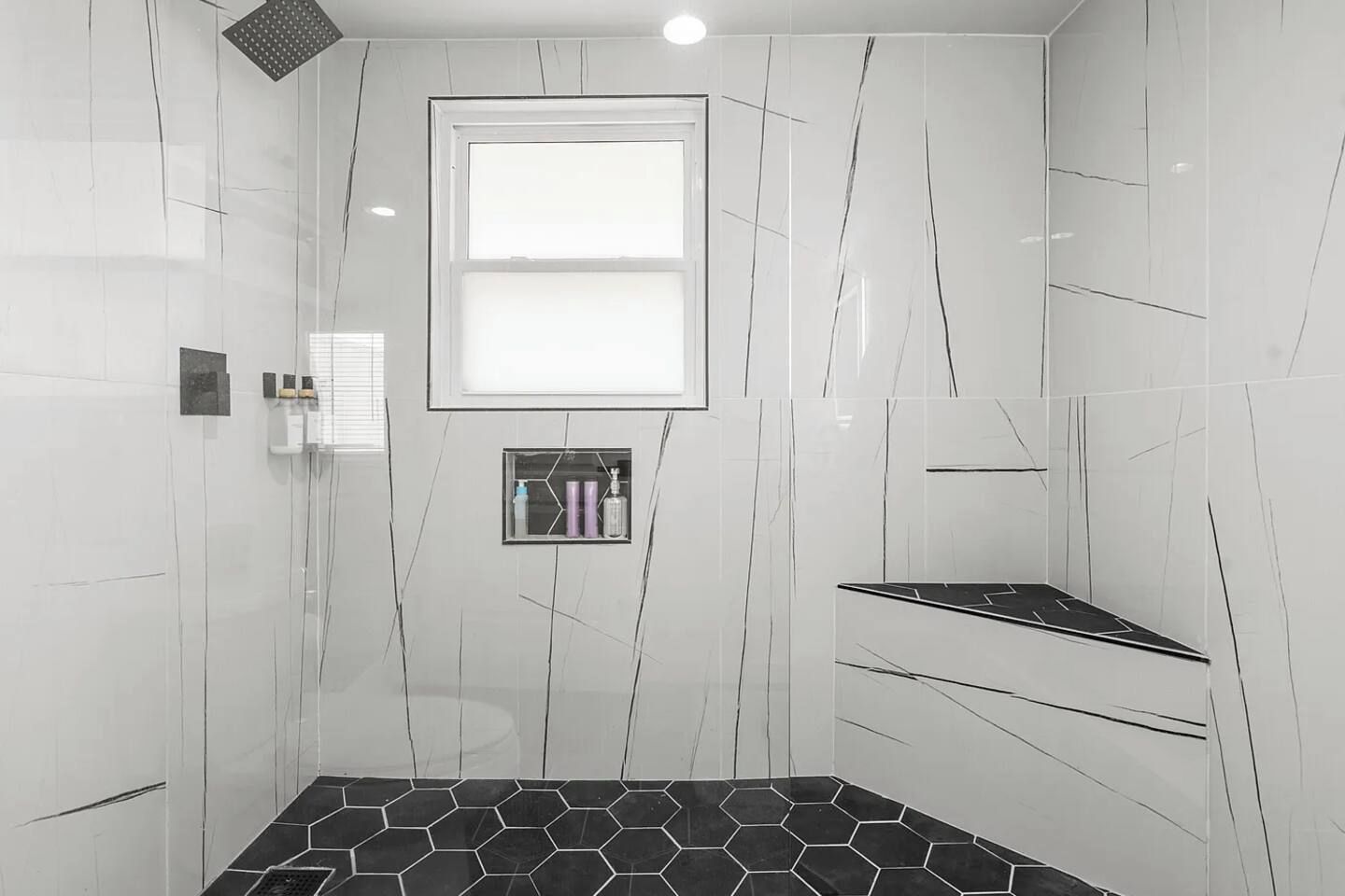 Een moderne badkamer met een douche, een raam en een inbouwplank met toiletartikelen.