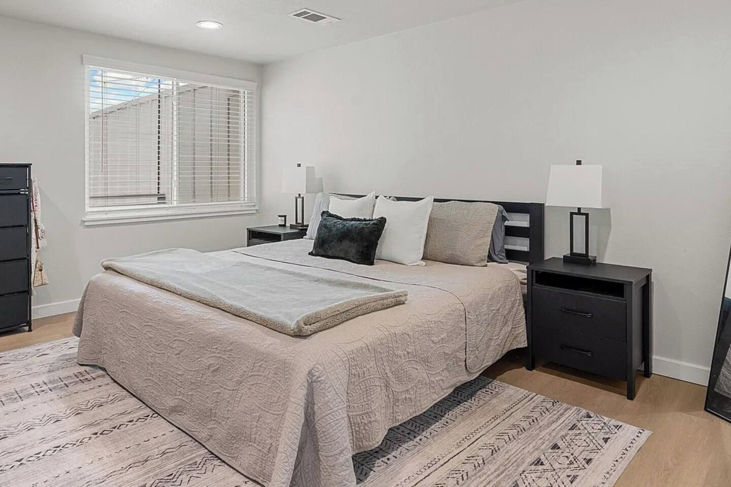 A bedroom with a bed, bedside tables, a lamp, a dresser, and a window with blinds.