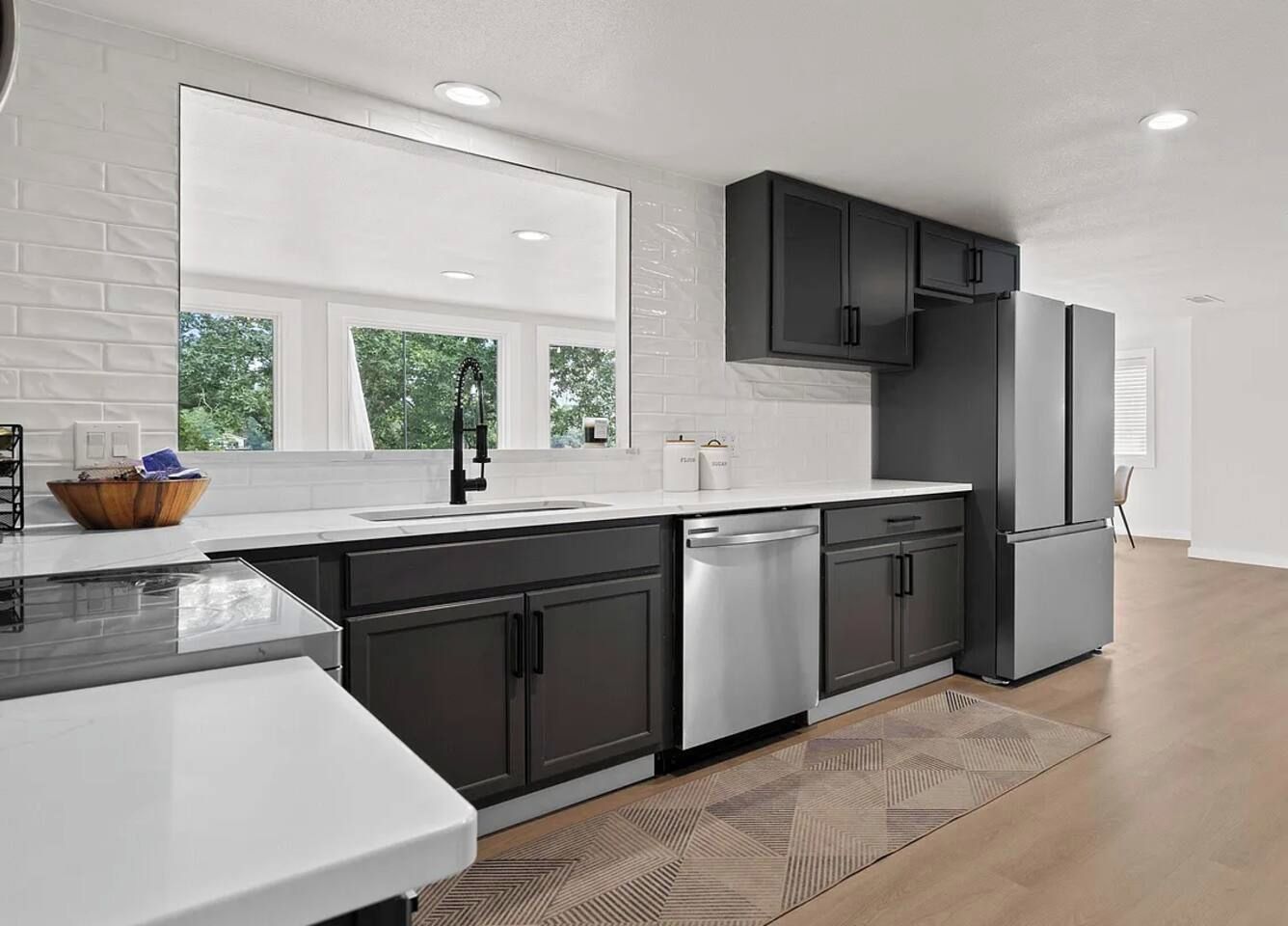 A modern kitchen with dark cabinets, stainless steel appliances, and a large window.