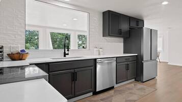 A modern kitchen with dark cabinets, stainless steel appliances, and a large window.