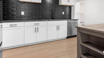 A kitchen with white cabinets, black backsplash, and wooden flooring.
