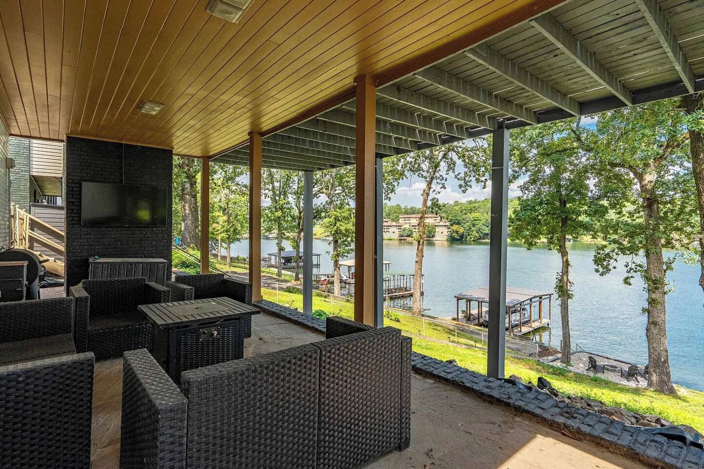 An outdoor seating area with wicker furniture, a flat-screen TV, and a view of a lake.