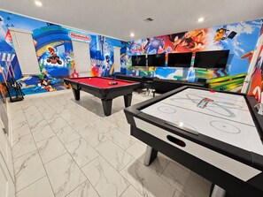 Sala de jogos com duas mesas de bilhar, uma mesa de sinuca e um mural com tema Nintendo.