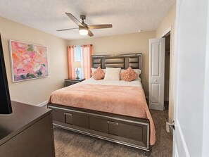 Ein Schlafzimmer mit Bett, Nachttisch, Deckenventilator, einem Gemälde und einer Tür.