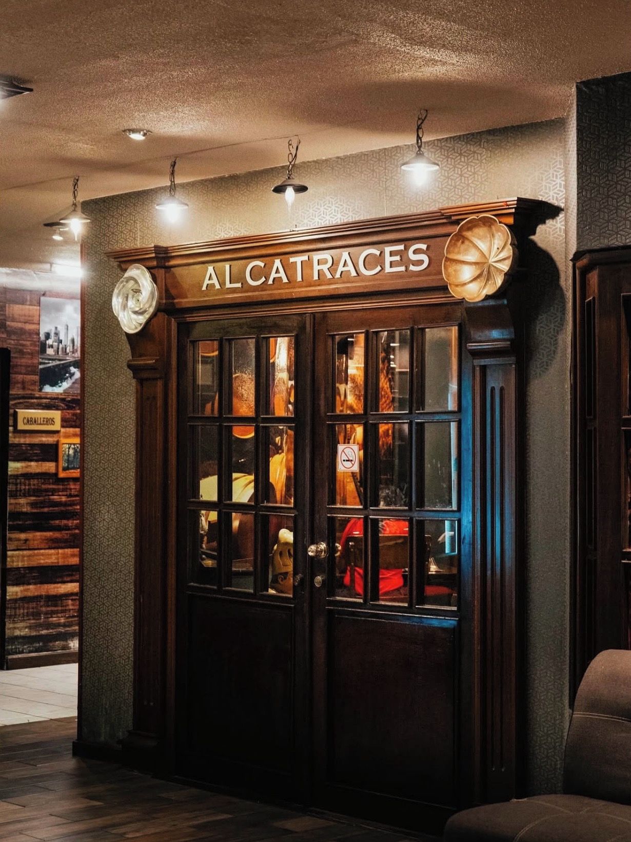 Tumma puinen sisäänkäynti, jossa on kyltti, jossa lukee ”ALCATRACES”, ja koristeellinen maapallo.