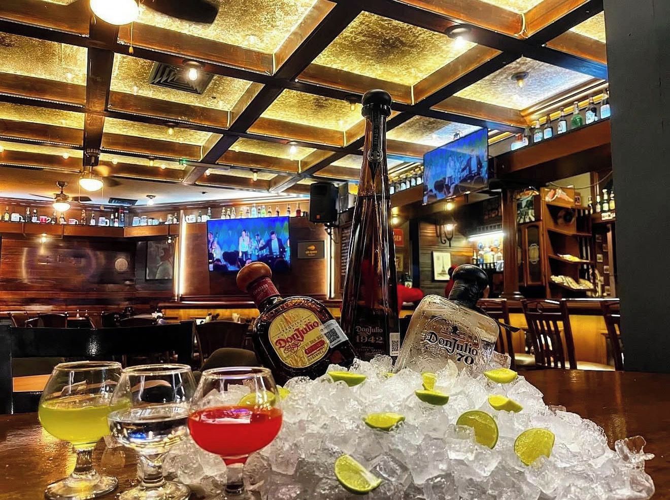 Una zona de bar con una botella de tequila Don Julio, hielo y vasos.