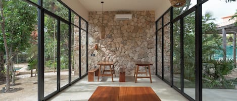 Una habitación amplia con pared de piedra, ventanas grandes y una mesa de madera.