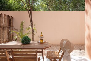 Une table en bois, avec une bouteille et des verres, entourée de chaises et d’une plante.