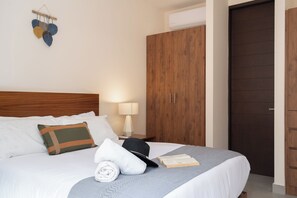 A hotel room with a bed, pillows, a bedside lamp, a wooden wardrobe, and a wall-mounted decorative item. - Resort-Style 2-Bedroom | Padel, Pool, Grill, Coworking Space (Tulum)
