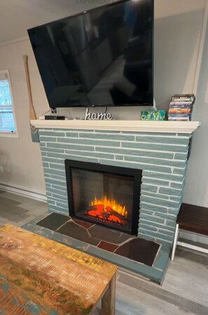 A fireplace with a television mounted above it, a stack of DVDs, and a word 'home' on the mantel. - Cozy 3 BR Cottage-Walk to Lake-Minutes to Skiing-Make Lasting Memories (Pocono Lake)