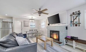 A modern living room with a fireplace, a flat-screen TV, and a ceiling fan. - Cozy 3 BR Cottage-Walk to Lake-Minutes to Skiing-Make Lasting Memories (Pocono Lake)
