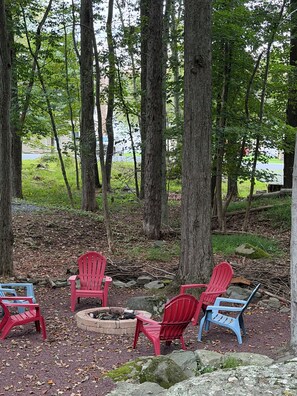 Ein bewaldetes Gebiet mit einem Feuerkorb und mehreren Adirondack-Stühlen.