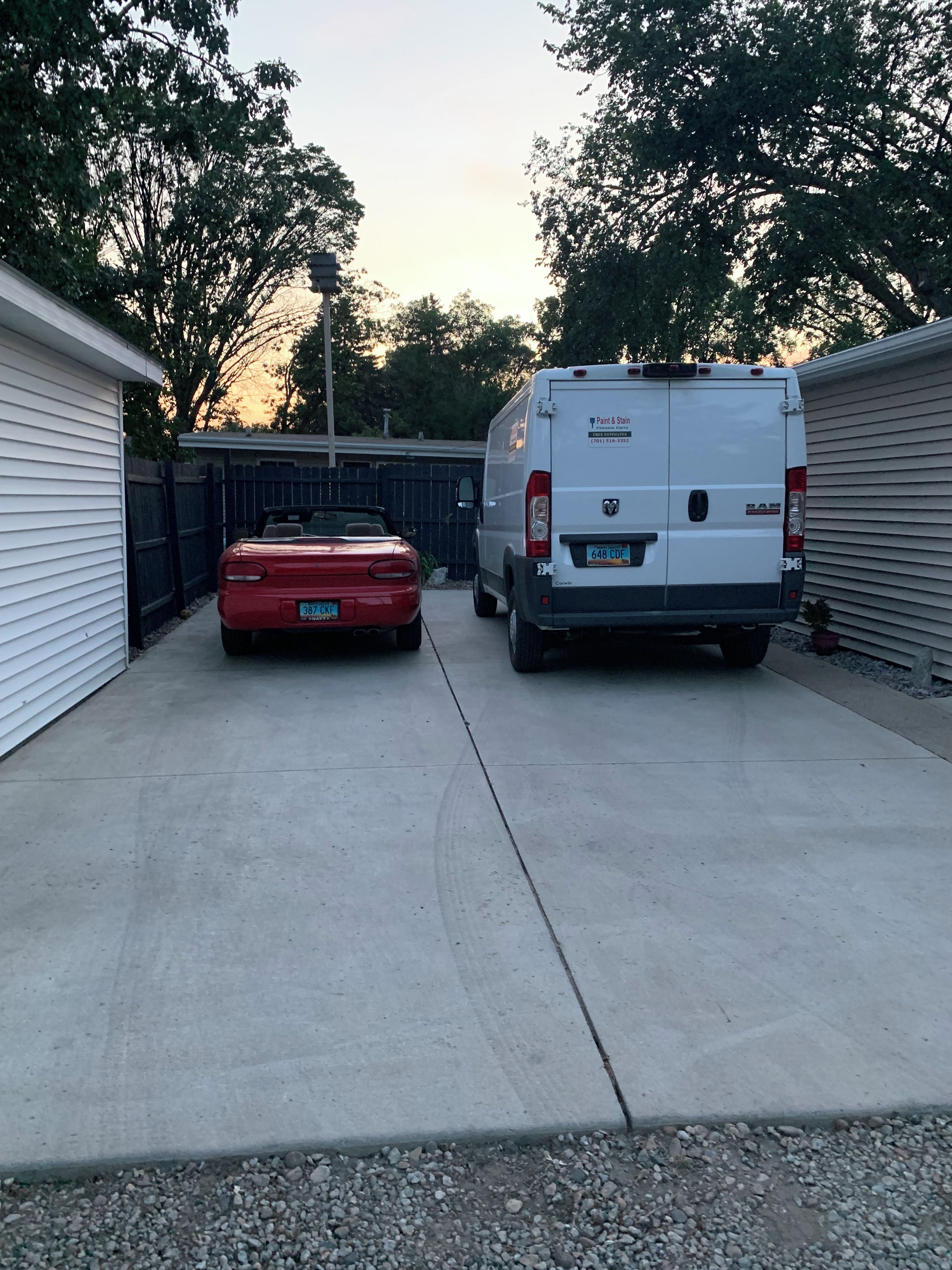 A driveway with a red car and a white van parked on the side.