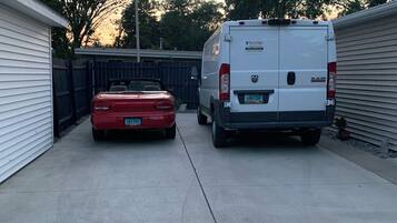 A driveway with a red car and a white van parked on the side.