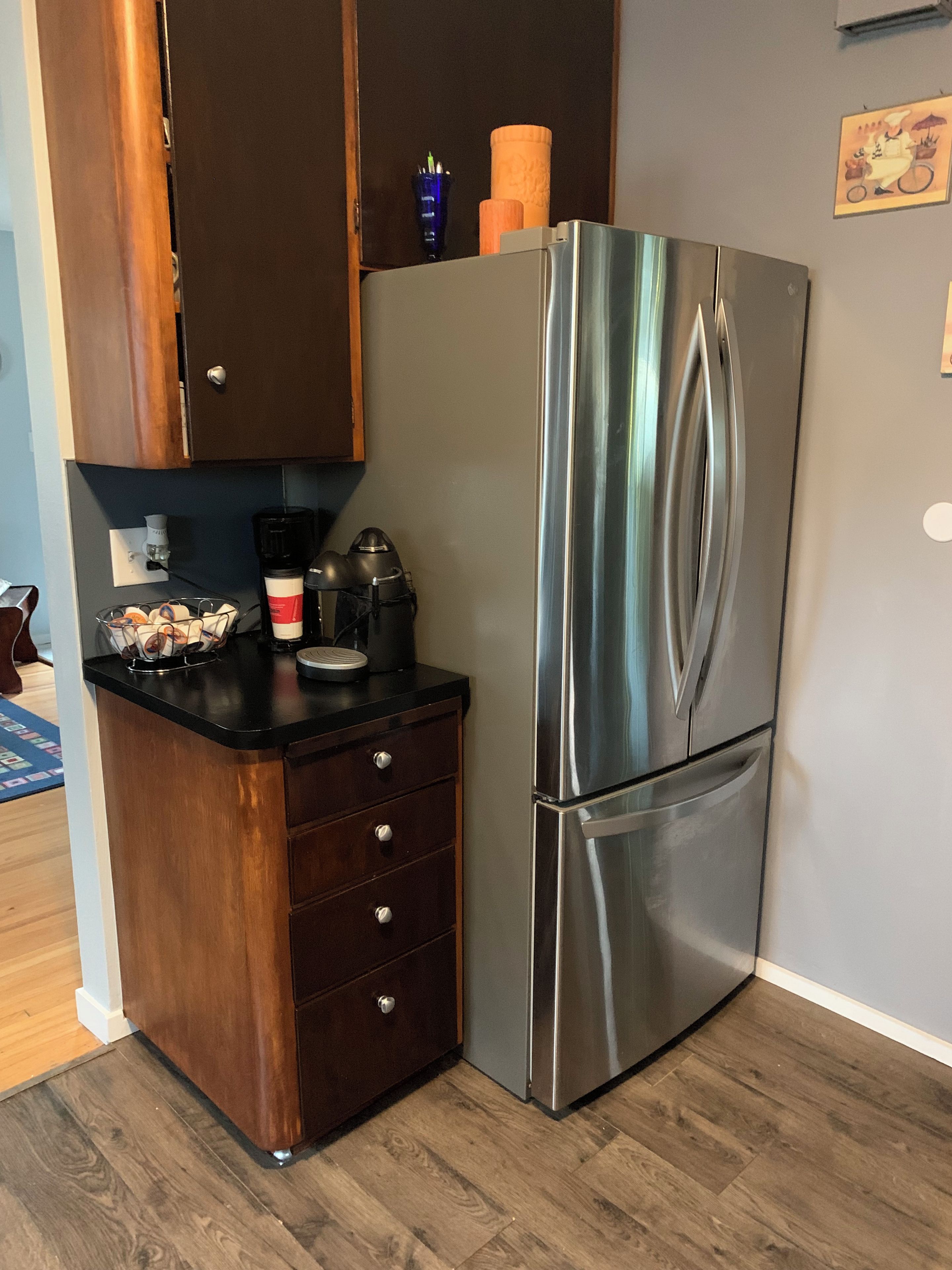A compact kitchen with a stainless steel refrigerator, wooden cabinets, and a black countertop.