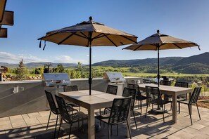 Une terrasse extérieure avec une table et des chaises, deux barbecues et des parasols pour faire de l’ombre.