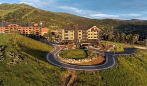 Een meerlaags gebouw met een gebogen oprit, omgeven door groen en heuvels.