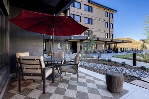 An outdoor seating area with a table and chairs, a red umbrella, and a modern building in the background. - AMB107 | Newest Luxury Complex | Close to Gondola | Winter Shuttle | A/C (Steamboat Springs)