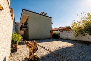 Une cour avec un sol de gravier, une sculpture en bois et un bâtiment doté d’un balcon.
