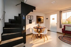 Eine Treppe führt zu einem Essbereich mit Tisch und Stühlen, einem an der Wand befestigten Fernseher und einem roten Sofa in einem hellen Raum mit Aussicht.