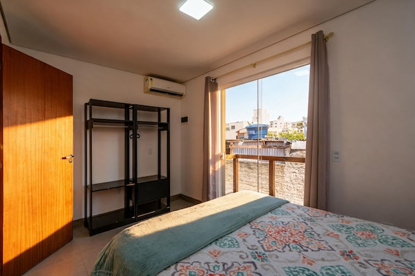 Ein Schlafzimmer mit Bett, Kleiderschrank, integriertem Bücherregal, Fenster mit Ausblick und Klimaanlage.