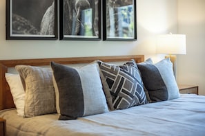 A neatly made bed with a wooden headboard, multiple pillows, and a framed picture above. - AMB109 | Newly Luxury Complex | Pool | Hot Tub | A/C | Winter Shuttle (Steamboat Springs)