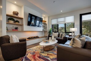 A modern living room with a flat-screen TV, comfortable seating, and a large window offering a view of the outdoors. - AMB109 | Newly Luxury Complex | Pool | Hot Tub | A/C | Winter Shuttle (Steamboat Springs)