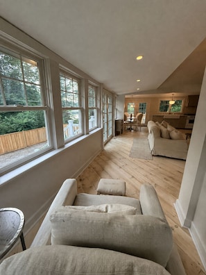 A spacious living area with a large window, a sofa, and a dining area. - The Flirt - Restored 1927 Cottage at Lake Waramaug (New Preston)