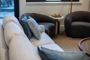 Una sala moderna con un sofá, dos sillones y una mesita auxiliar con un objeto decorativo.