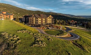 Hotel com vários andares e um pátio ajardinado, localizado em uma encosta com vista para montanhas ao redor.