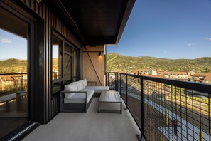 A balcony with a sofa and a table, overlooking a town and hills. - AMB210 | Steamboats Newest Luxury Complex | A/C | Hot Tub | Pool | Walk to Skiin (Steamboat Springs)
