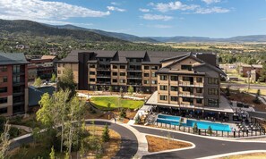 A multi-story hotel with a swimming pool, surrounded by a landscaped area and a view of distant mountains. - AMB210 | Steamboats Newest Luxury Complex | A/C | Hot Tub | Pool | Walk to Skiin (Steamboat Springs)