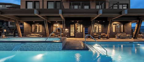 Modern mountain property featuring outdoor pools and covered lounge areas, captured during the tranquil twilight hour.