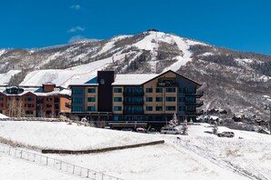 A multi-story hotel with a ski slope in the background. - AMB305 | New Luxury Complex | Pool | Hot Tub | A/C | Walk to Slopes (Steamboat Springs)