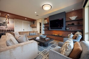 A modern living room with a fireplace, a flat-screen TV, and a dining area with a chandelier. - AMB308 | Newest Luxury Complex | A/C | Pool | Winter Shuttle (Steamboat Springs)