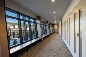 Un couloir d’hôtel avec de grandes fenêtres, un sol recouvert de moquette et une rangée de portes sur le côté droit.