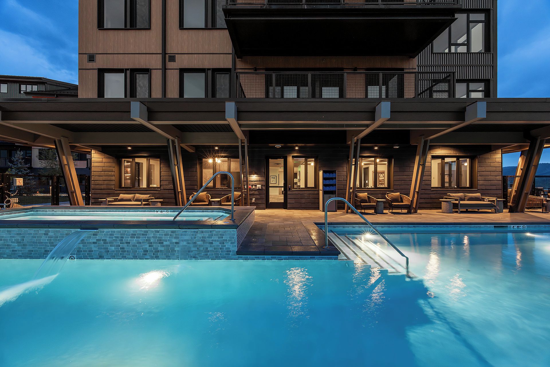 Modern mountain property featuring outdoor pools and covered lounge areas, captured during the tranquil twilight hour.