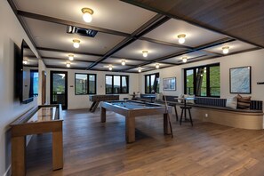 Ein geräumiges Zimmer mit Billardtisch, einer Sitzecke und großen Fenstern mit Blick ins Freie.