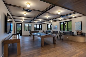 Ein geräumiges Zimmer mit Billardtisch, einer Sitzecke und großen Fenstern mit Blick ins Freie.